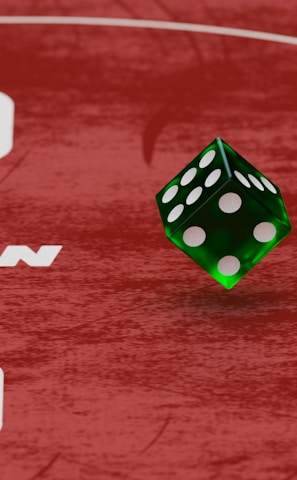 Two green dice with rounded edges are positioned on a red surface that seems to be part of a game board. The surface has white text and numbers on it, including the word 'LUCKYTOPSPIN' in capital letters.